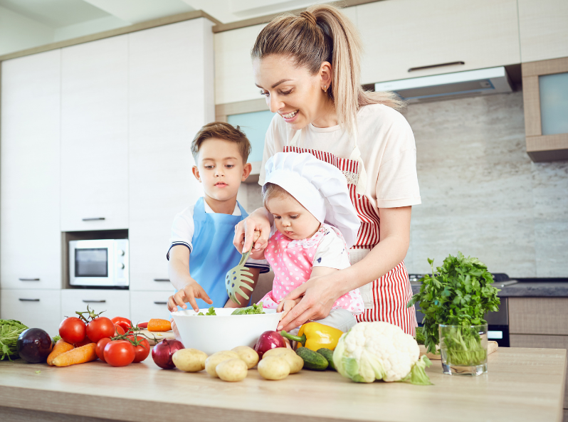 Mama gotuje razem z synkiem i córeczką w kuchni, przygotowując sałatkę z warzyw